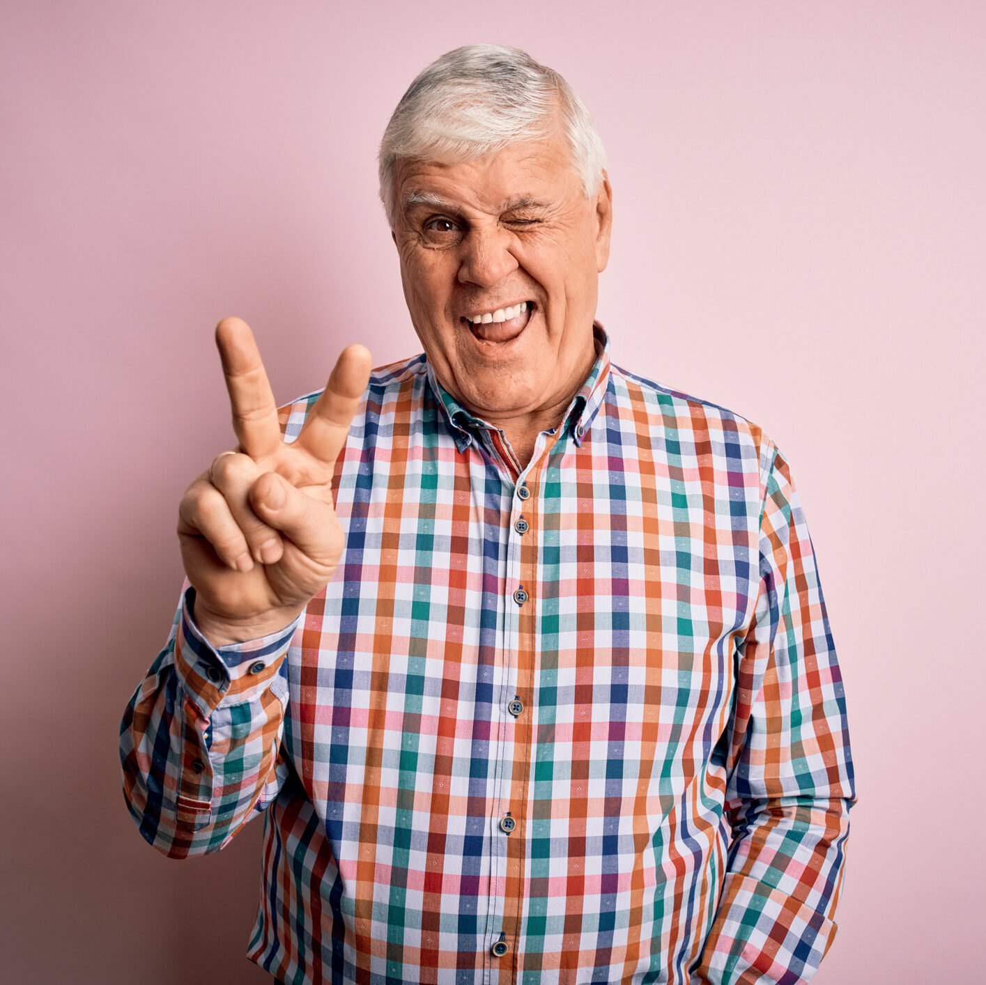 Senior handsome hoary man wearing casual colorful shirt over isolated pink background smiling with happy face winking at the camera doing victory sign with fingers. Number two.